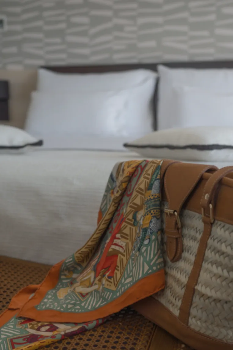 Foulard de soie et panier en osier au pied du lit d'une chambre d'hôtel