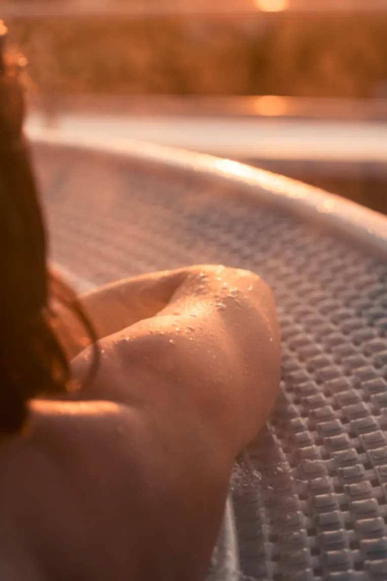 Main effleurant l'eau d'un jacuzzi dans la lumière dorée du soir